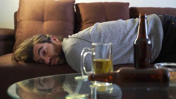 Young Man Having Hangover After New Year Party Sleeping with Chaos on Sofa alt
