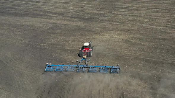 Aerial Shot of a Red Tractor Cultivating Brown Earth in Sunny Spring Autumn Weather alt