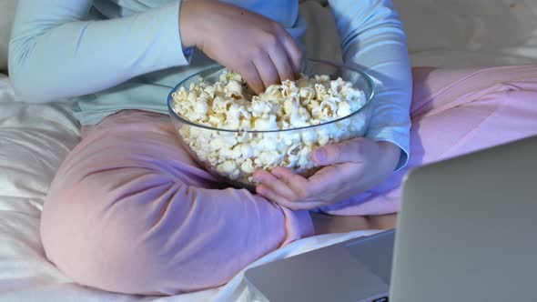 Child eats popcorn out of a clear dish while watching a movie.