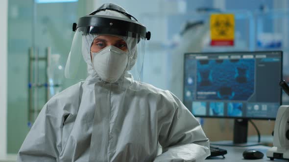 Tired Microbiologist in Coverall Sitting in Laboratory Looking at Camera alt