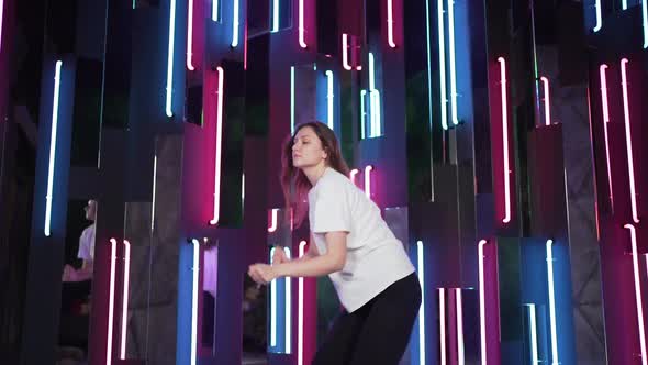 The Person Dances at Night in a Colorful Neon Room with Mirrors and Reflections