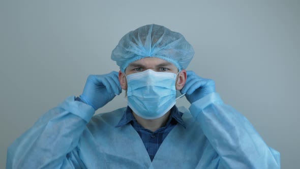 Male doctor in protective gear puts on medical face mask before surgical treatment. alt