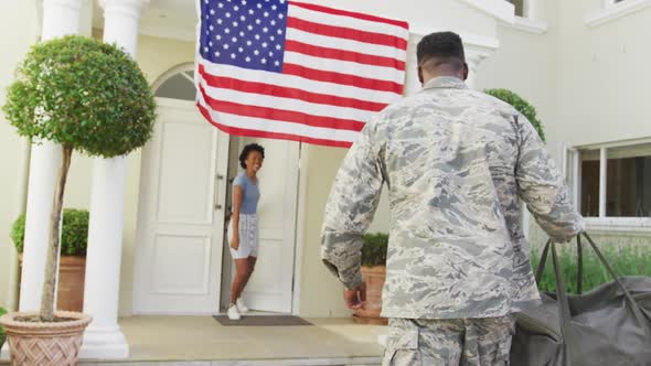 African american male soldier embracing his smiling wife over american flag alt