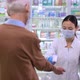 Young Asian Woman Taking Temperature of Caucasian Senior Man in Pharmacy at Entrance - VideoHive Item for Sale