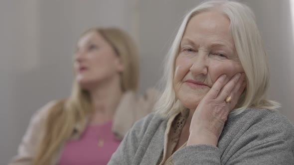 Closeup Portrait of Sad Unhappy Senior Caucasian Woman with Grey Hair Looking at Camera As Blurred alt
