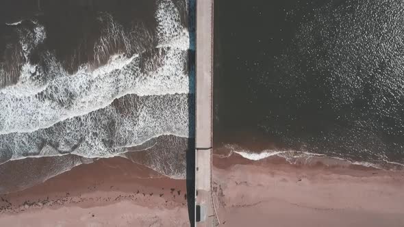 Aerial birds eye view drone footage of a waves crashing onto the beach against a pier, Roker Beach, alt