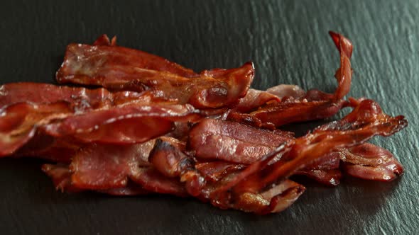 Super Slow Motion Shot of Roasted Bacon Slices Falling on Black Table at 1000 Fps alt