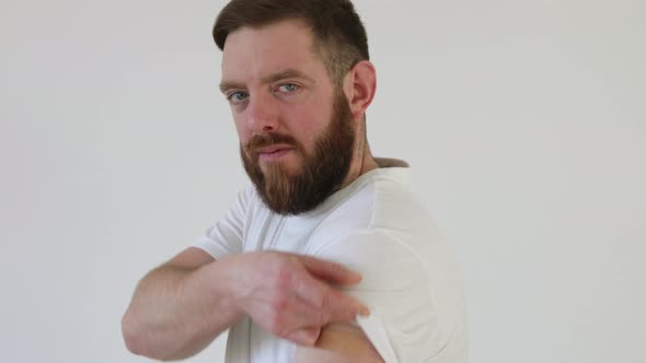 Portrait of smiling bearded man after getting a vaccine. Male holding up his white shirt sleeve