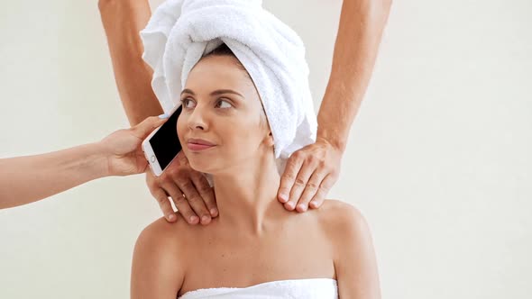 Hands Doing Massage Giving Phone and Cup of Coffee to Young Beautiful Naked Girl in Towel Over White alt