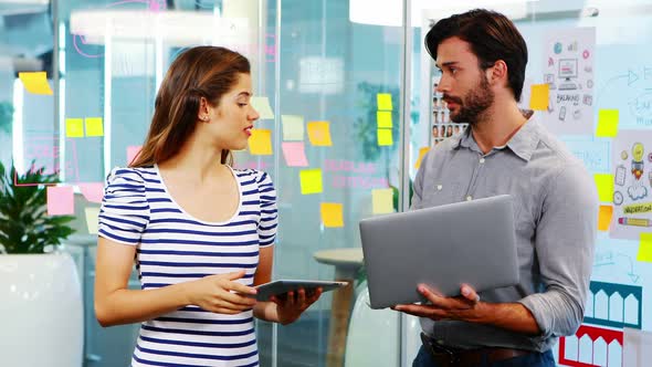 Male and female executives discussing over electronic devices alt