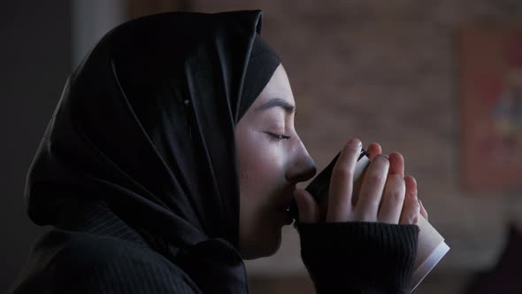 Young Muslim Woman in Hijab Drinking Tea or Coffee and Looking Away Thinking Solving Problem Serious