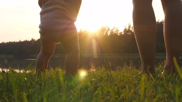 Parents and Baby Standing Barefoot on Grass at Sunset By the Lake. Single Parent Concept.  alt