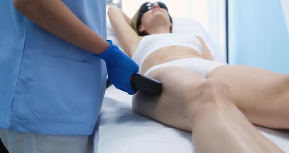 Young Woman Undergoes Procedure for Laser Hair Removal of Legs in Beauty Salon alt