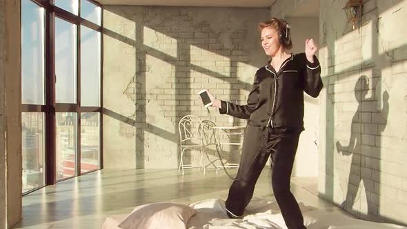 Happy Woman Girl in Headphones Listening To Music and Dancing on the Bed