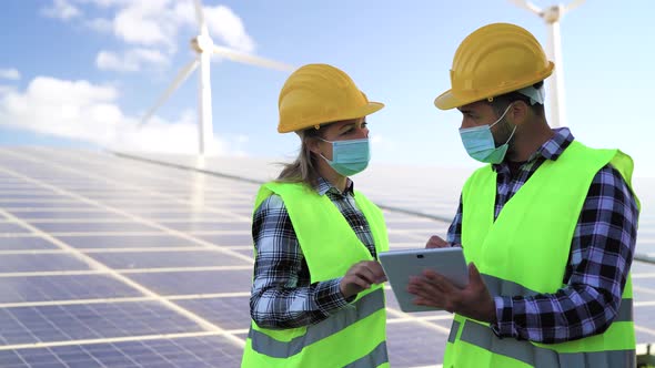 People working for alternative energy with wind turbine and solar panel while wearing face mask alt
