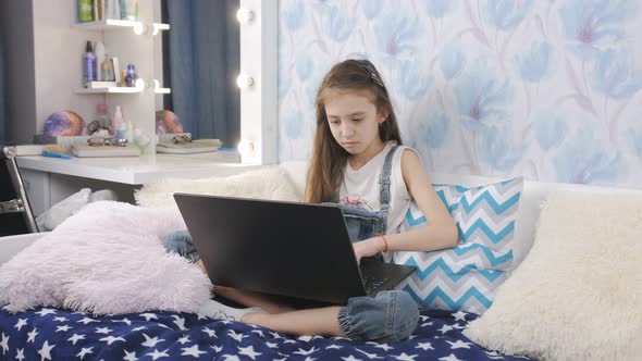 A Teenage Girl Uses a Laptop to Do Homework While Sitting on the Bed