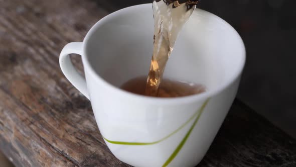 Slow motion shot of pouring a cup of tea in a white mug on a wooden table. alt