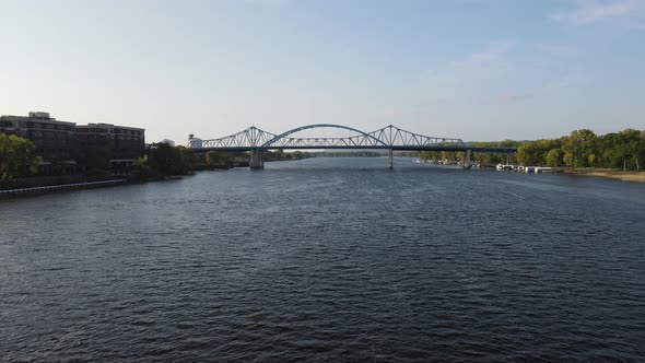 Flyover down Mississippi River toward two big blue bridges with sun reflecting off the water.