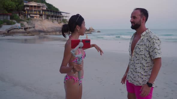 Young Asian Live Blogger Streamer Interviewing Tourist Caucasian Man at Exotic Island Beach on alt