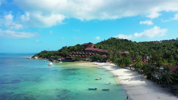Anchored boats on calm turquoise lagoon in front of white sandy beach with palm trees near holiday r alt