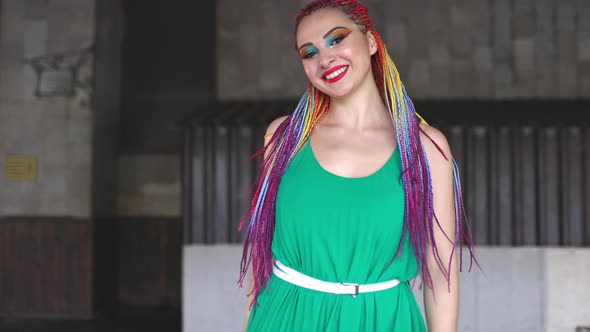 A Girl with Makeup and Multicolored African Braids in a Green Dress Smiles Cutely Walking Along the alt