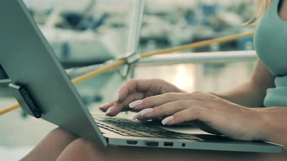 Close Up of Woman's Hands Typing on a Laptop Near Water alt