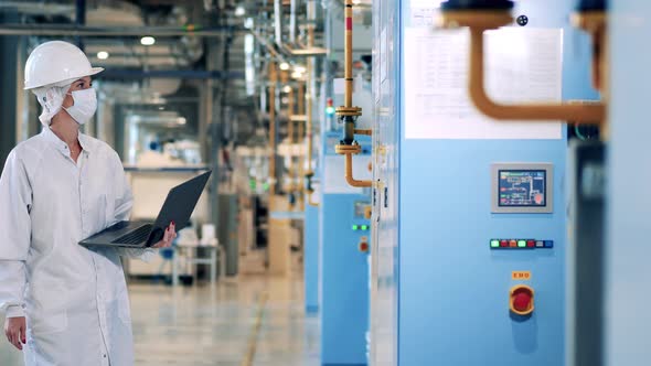 Female Engineer with a Laptop Comes Closer to the Factory Machines alt
