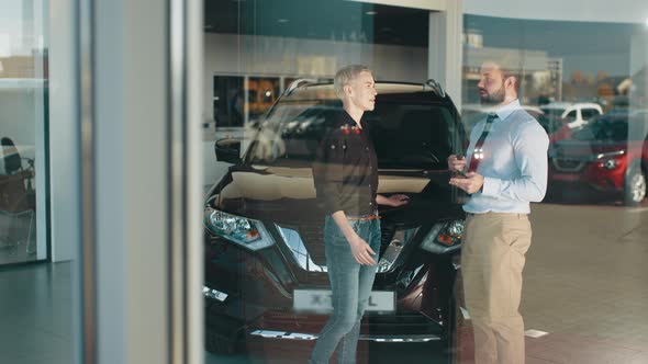 Adult Female Customer and Smiling Male Car Dealer Standing at Car Salon Interior alt