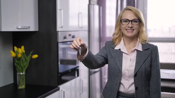 Attractive Senior Realtor Offering Keys To Camera alt