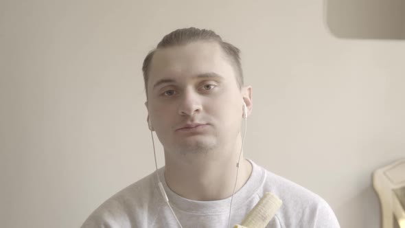 Close-up of Brown-eyed Brunette Man Eating Banana. Portrait of Young Caucasian Guy in Earphones alt