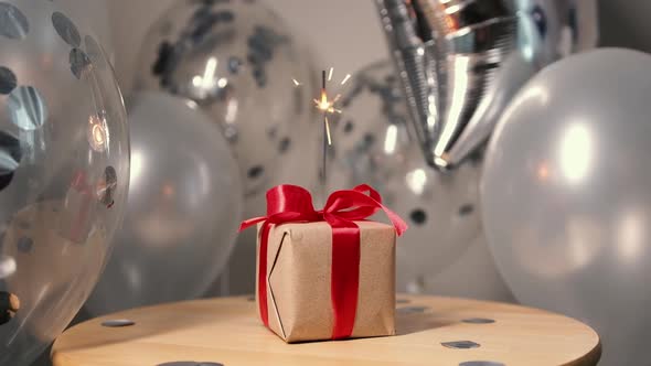Gift Box with a Red Ribbon and a Bow with Sparklers Balloons on the Background