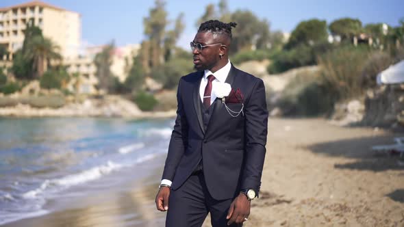 Portrait of Thoughtful Lonely African American Groom in Elegant Suit Strolling on Sandy Beach in alt