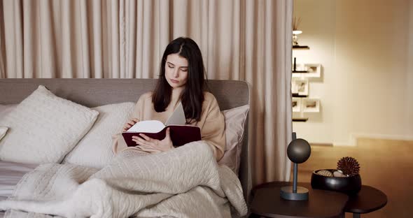 Woman Relaxing in Bed and Reading a Book in the Bedroom in the Modern House alt