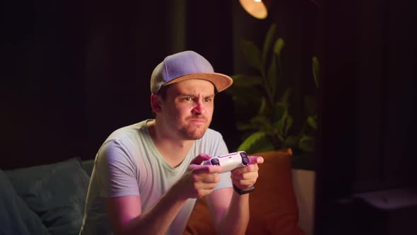 Young Man Sitting on Sofa and Playing Video Game on TV in Living Room alt
