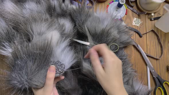 Top View of Seamstress Hands Who Sew Patterned Clasp on Grey Fluffy Fur