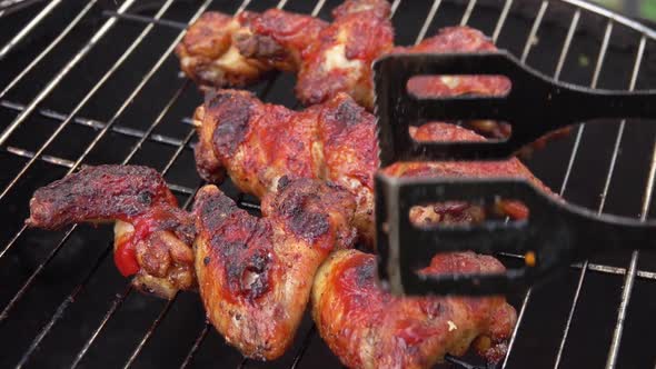 Closeup of the Chicken Wings Rotated on the Grill Grid with Metal Tongs alt
