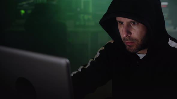 Portrait of Mysterious Hooded Hacker Sitting at Desk and Breaking Into Government Data Servers in alt