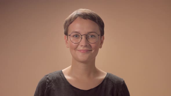 Caucasian Woman with Short Haircut Wears Glasses in Studio on Beige Background