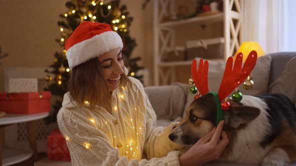 Broll of Smiling Tender and Affectionate Woman in Santa Hat Putts on Reindeer Antlers Headband on alt