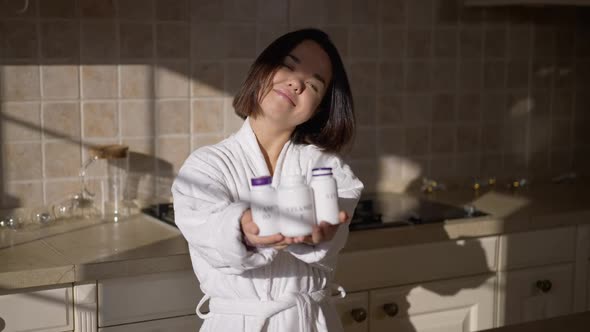 Smiling Adult Little Woman Posing with Vitamin Bottles in Kitchen at Home on Sunny Morning alt