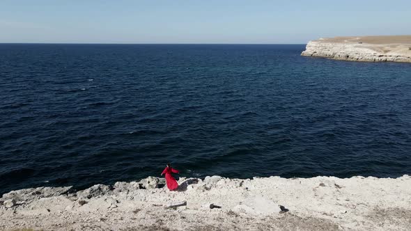Brunette Woman in a Red Long Dress Walk on the Edge of a Cliff By the Sea alt