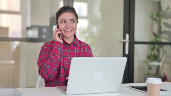Indian Woman Talking on Smartphone While Using Laptop alt