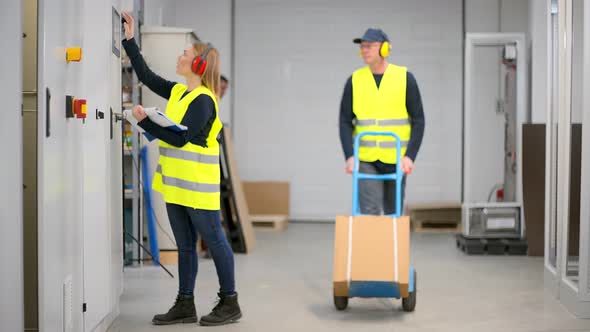 Electrician checking settings of machine, man passing by with pushcart alt