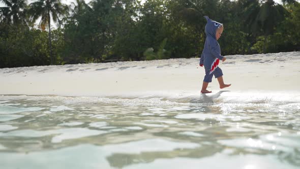 A Child in a Shark Costume Runs Along a Tropical Beach Along the Ocean alt