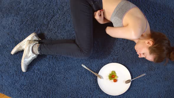 Sad Woman Having Anorexia Nervosa Having Small Green Vegetable and Tomato on Plate Lying on Floor alt