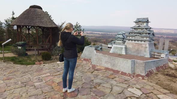 Woman Takes a Photo Near a Miniature Chinese Japanese Pagoda. Park of Miniatures. alt
