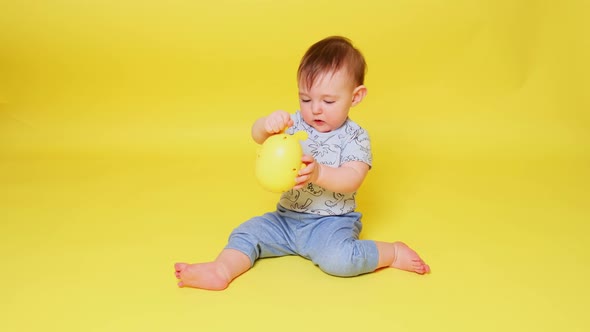 Happy toddler baby boy is playing with a toy on a studio yellow background. Smiling child