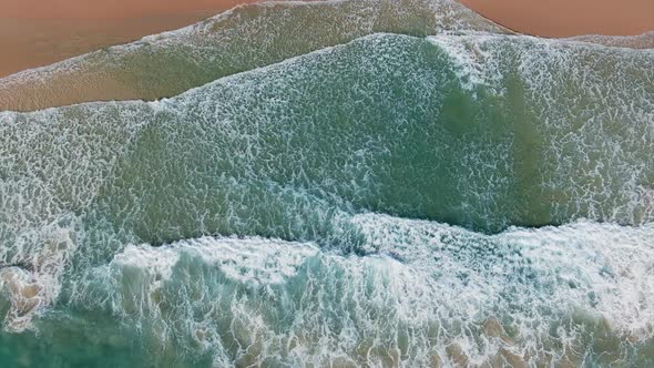 Drone view into deep blue ocean water and foamy waves to the beach.