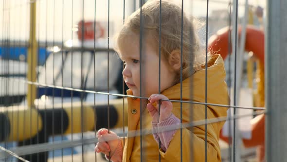 Little Girl Looks at Ships in Marina or Bay Through Lattice
