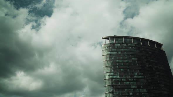 Cloud reflections on the glasses of a high rise big building on a cloudy day while a plane passes by alt